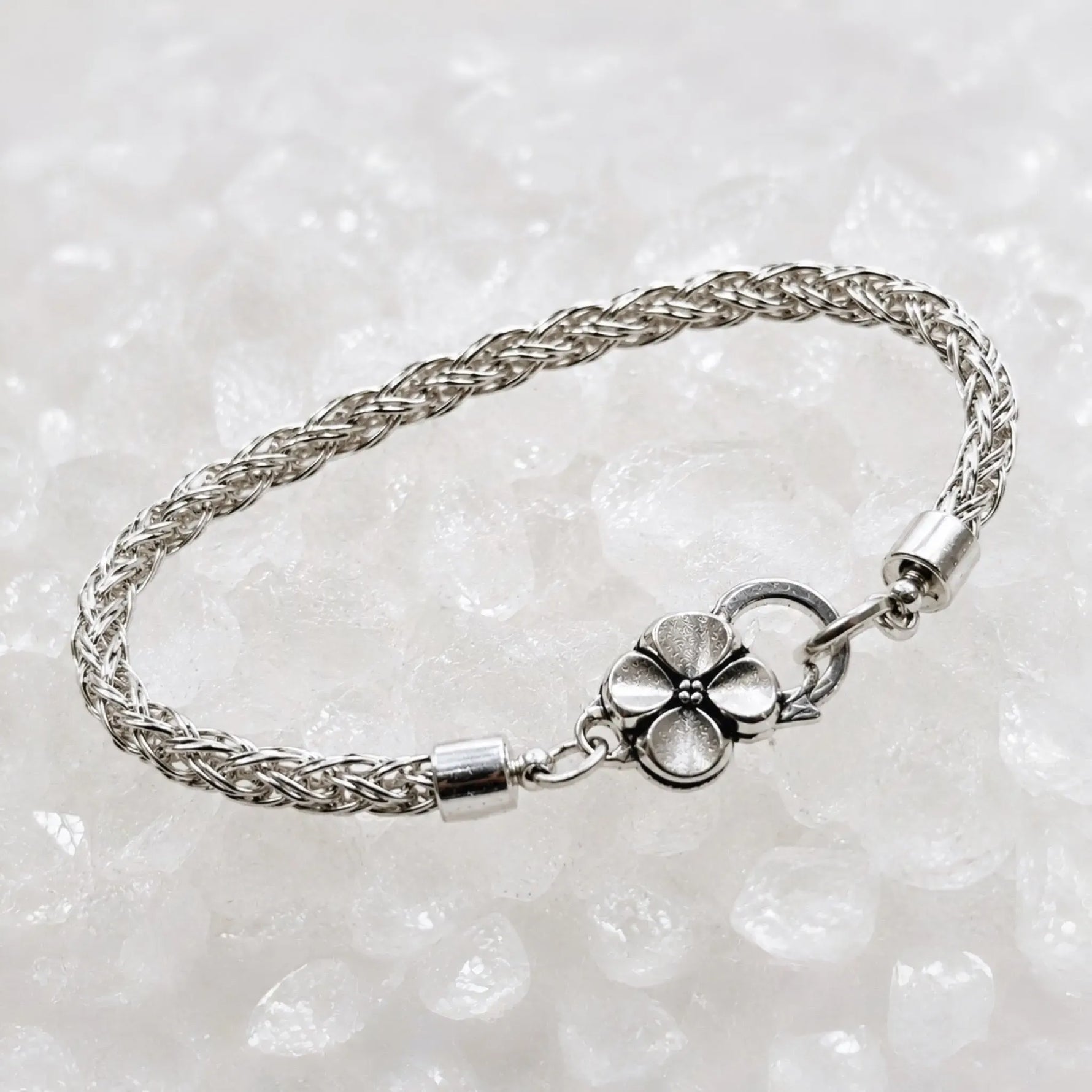 Three-quarter view of the Gemma handwoven .999 fine silver bracelet showcasing the woven silver chain and sterling silver apple blossom clasp on white quartz.