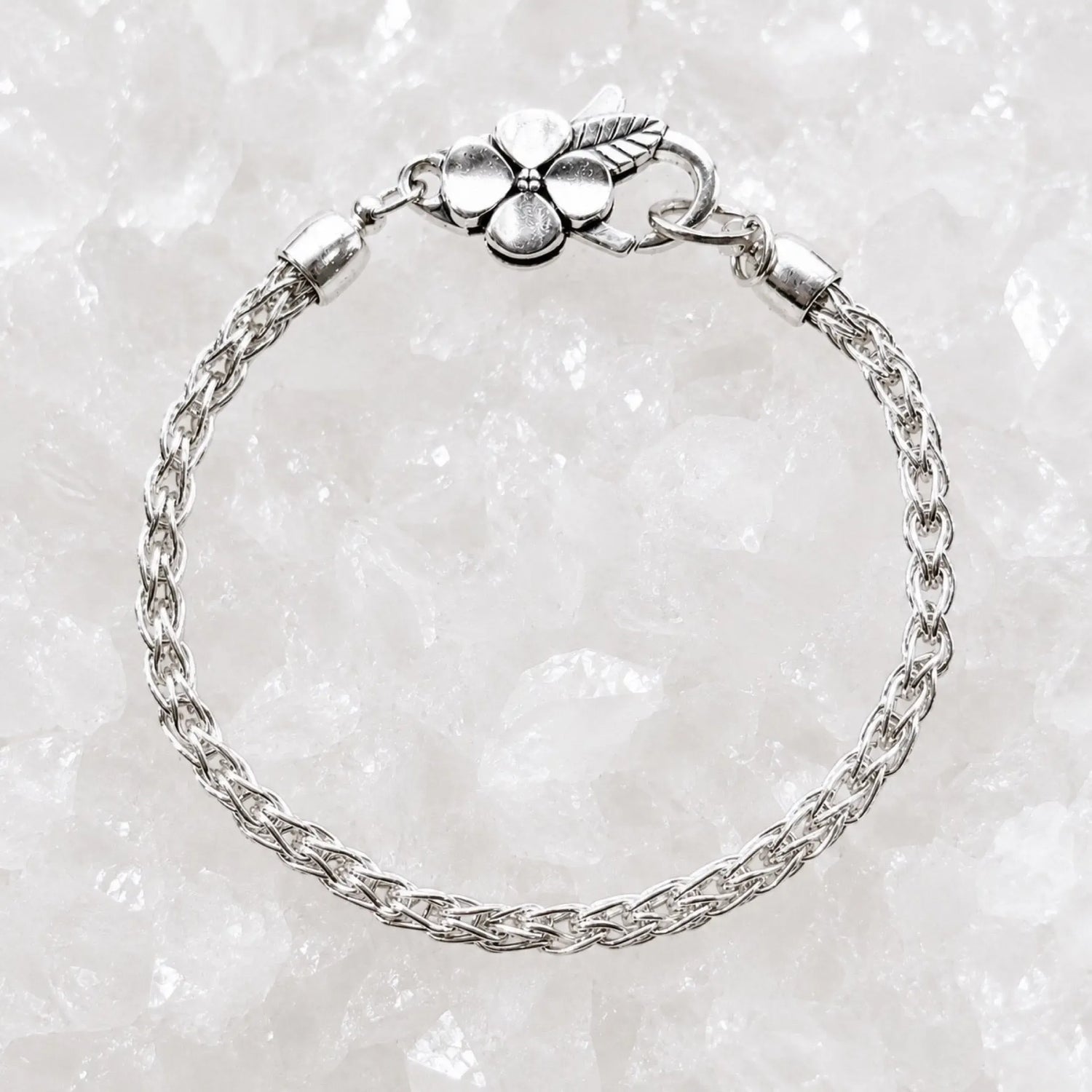 Gemma handwoven .999 fine silver bracelet with sterling silver apple blossom clasp displayed on a luminous white quartz crystal background.
