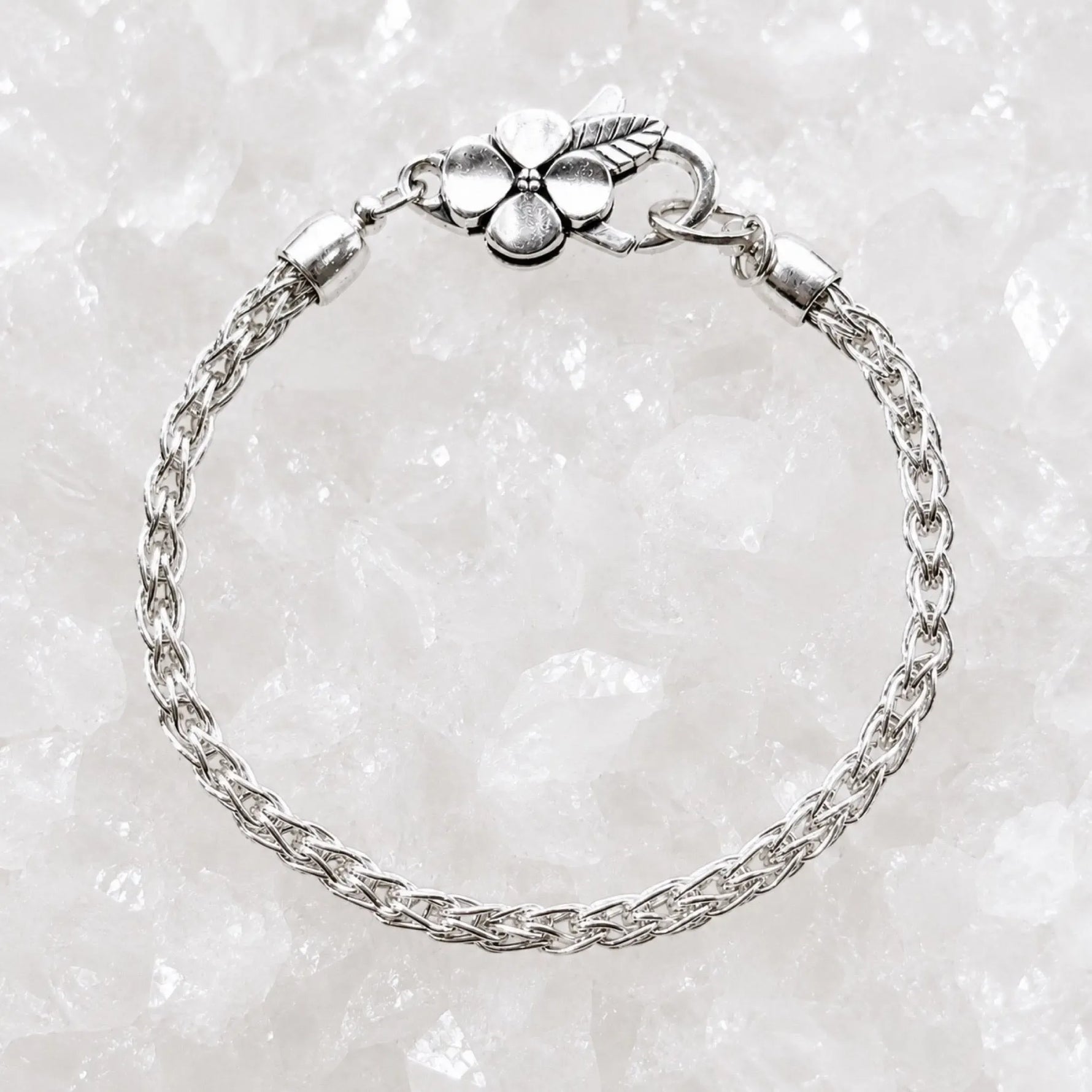 Gemma handwoven .999 fine silver bracelet with sterling silver apple blossom clasp displayed on a luminous white quartz crystal background.