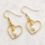Harlow Gold Heart Earrings with cream Swarovski® Crystal Pearls and honey opal gemstones on Carabella white quartz background.