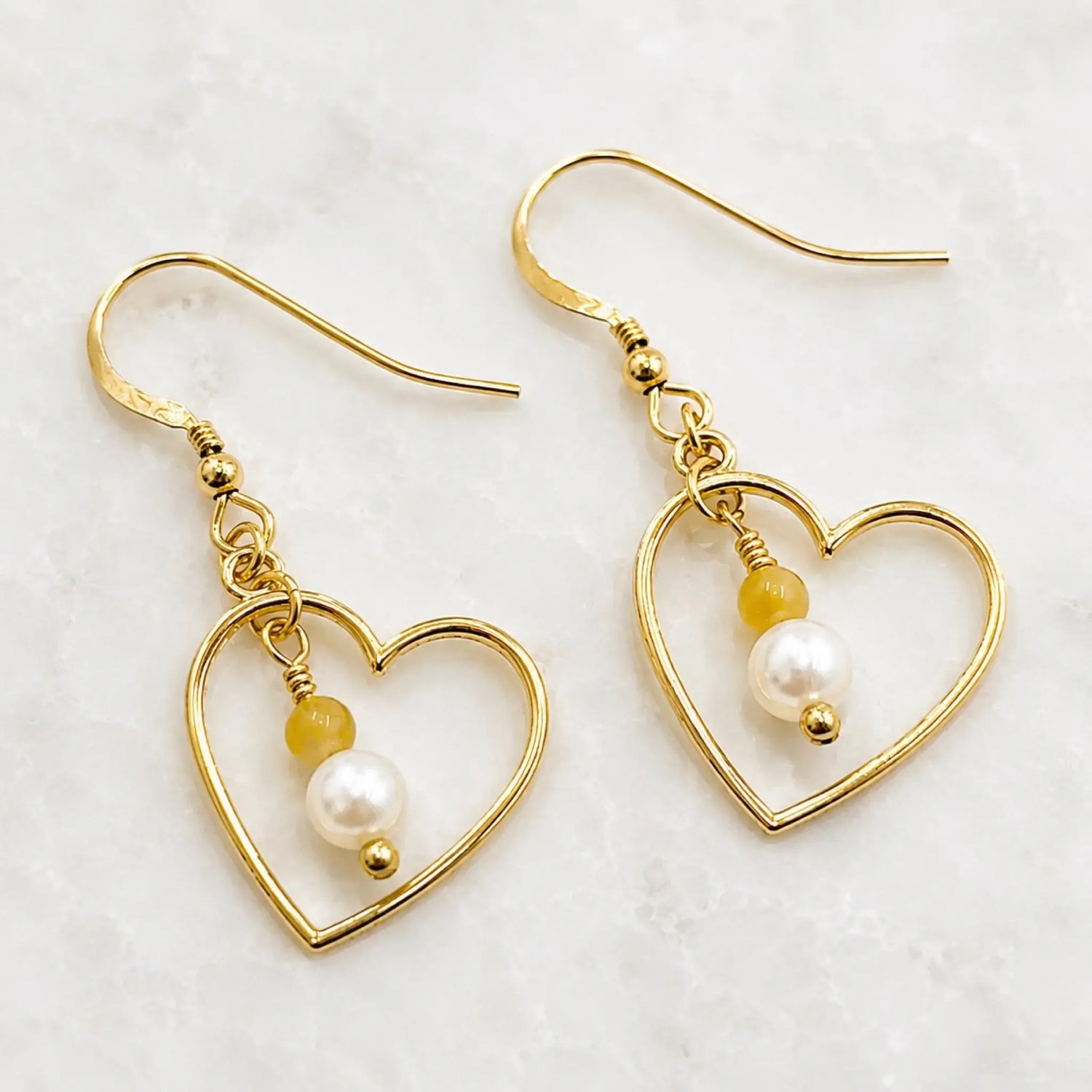 Harlow Gold Heart Earrings with cream Swarovski® Crystal Pearls and honey opal gemstones on Carabella white quartz background.