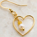 Macro detail of Harlow Gold Heart Earrings showcasing the handcrafted open heart, cream Swarovski® Crystal Pearl, honey opal gemstone, gold wire wrapping and polished gold details.