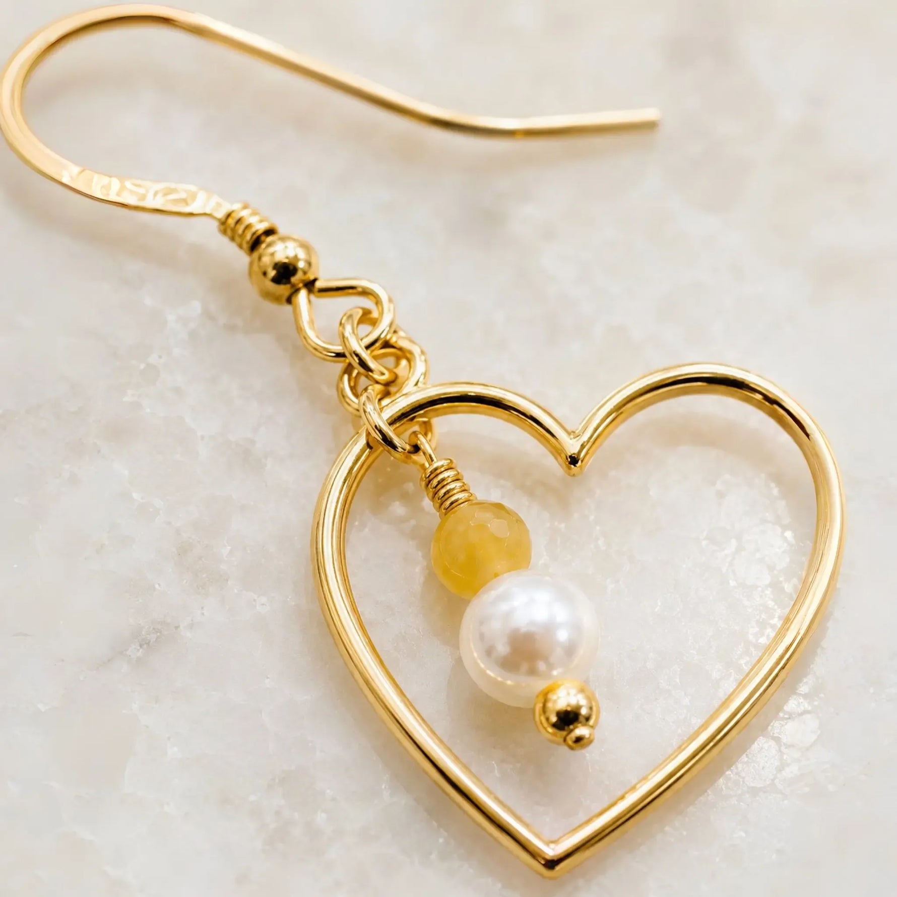 Macro detail of Harlow Gold Heart Earrings showcasing the handcrafted open heart, cream Swarovski® Crystal Pearl, honey opal gemstone, gold wire wrapping and polished gold details.