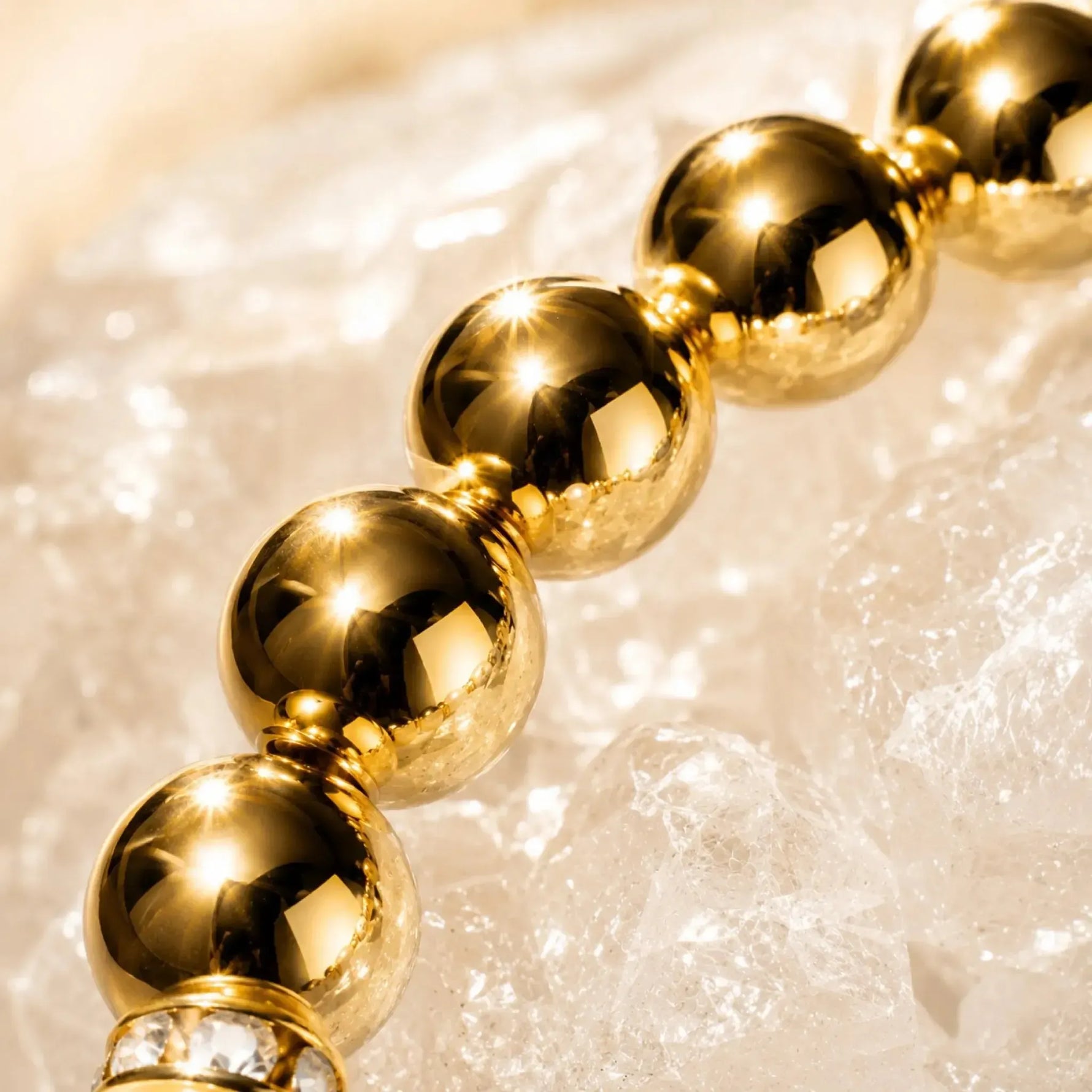 Luxury macro photograph of highly polished gold-plated hematite gemstones from the Imperial Blossom Bracelet, showcasing brilliant reflective surfaces and crystal accents against a sparkling quartz crystal backdrop.