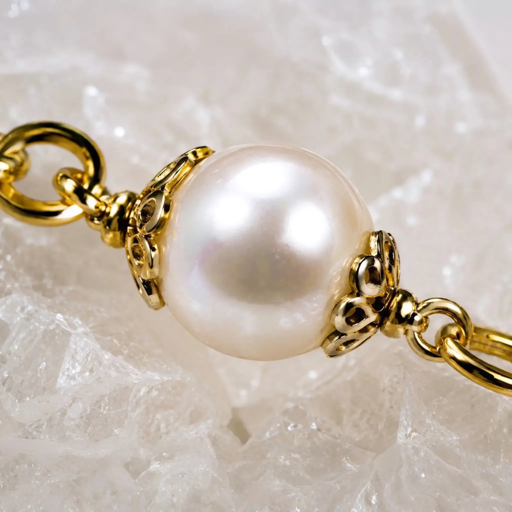 Imperial Blossom Swarovski® Crystal Pearl Necklace detail featuring a luminous pearl, gold-plated bead caps, and gold chain links on a white quartz crystal background.