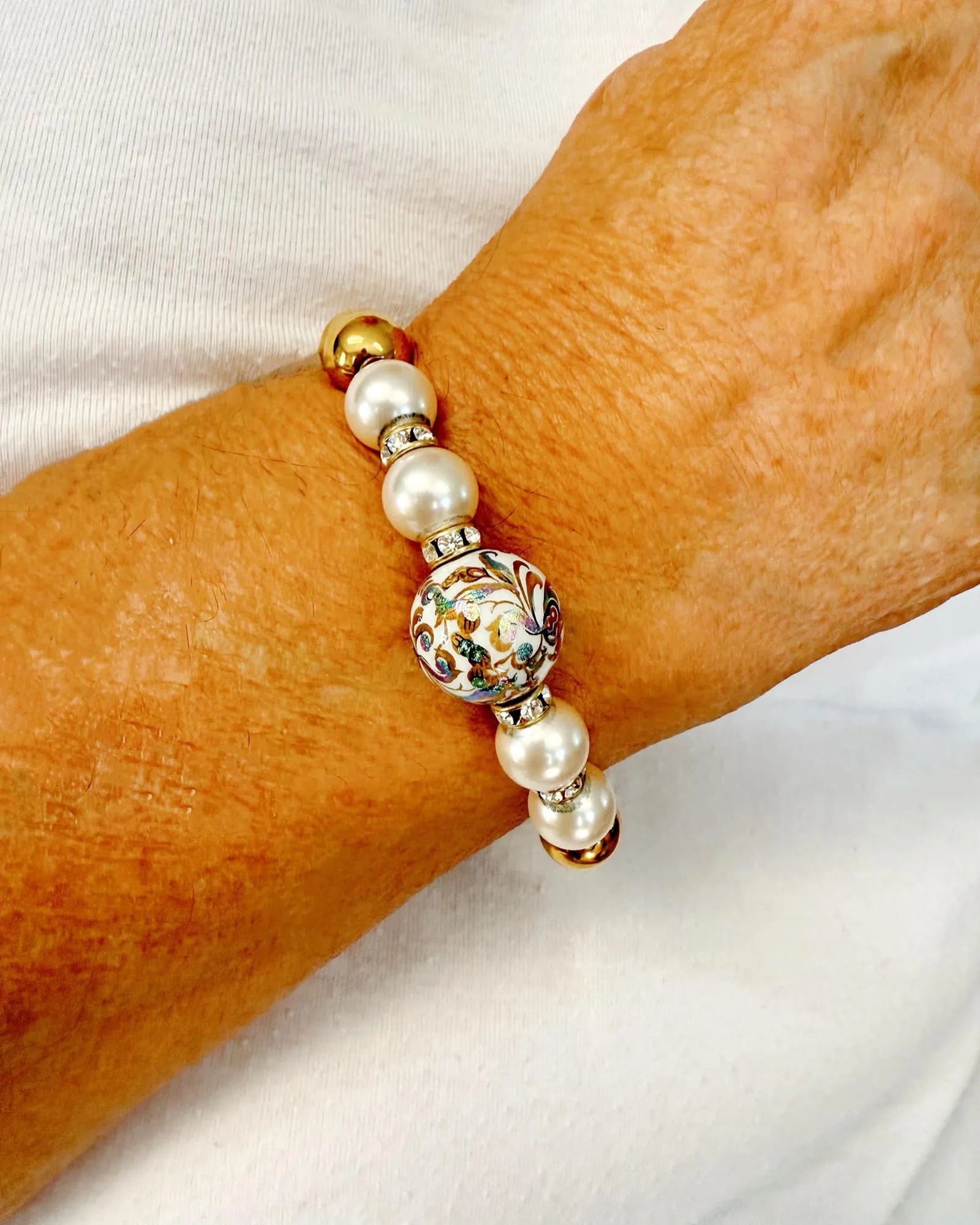 Imperial Blossom Stretch Bracelet worn on wrist, featuring a rare Japanese Tensha bead with floral artwork, Austrian Crystal cream rose pearls, sparkling rondelles, and gold-plated hematite. Handcrafted in Canada by Carabella by Cheryl.