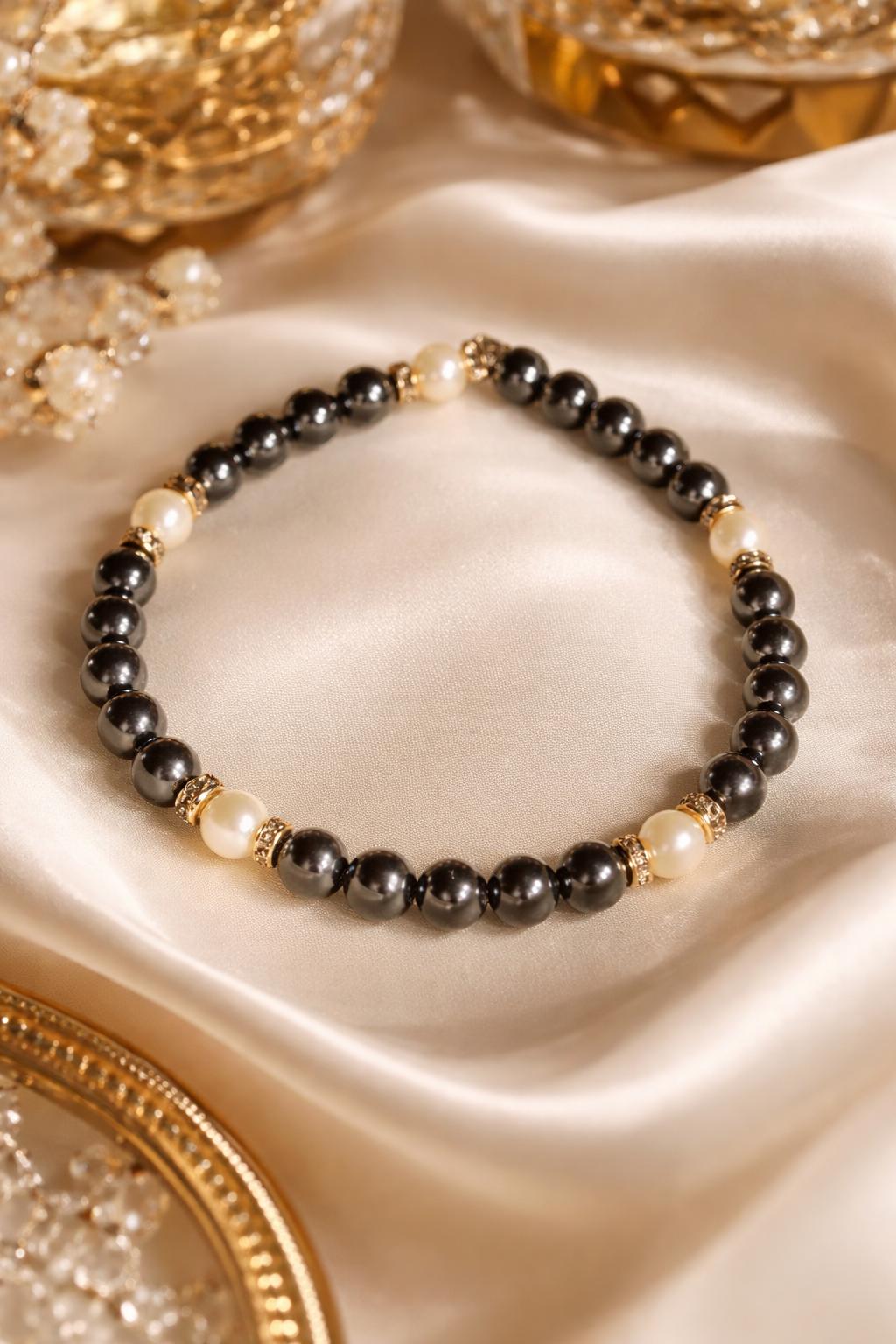 Jan Black Pearl Bracelet with luminous white pearls and deep black crystal tones, finished with warm gold accents, styled on soft silk for a refined, quiet luxury look.