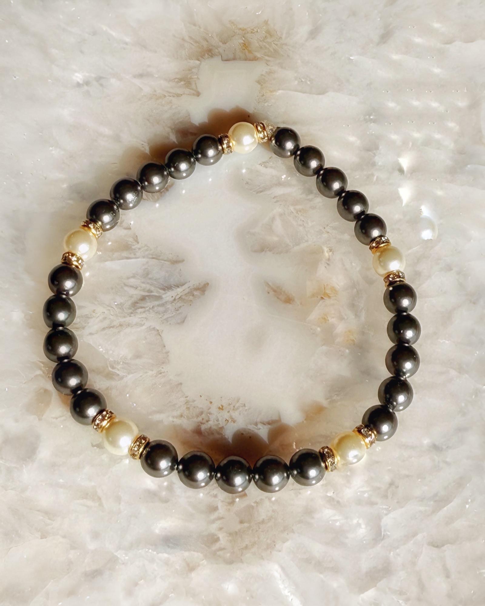 Jan Black Pearl Bracelet featuring black crystal pearls, white pearl accents, and warm gold detailing, photographed on natural stone for a timeless, polished aesthetic.