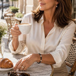 Elegant woman wearing the Jan Swarovski® Crystal Pearl Bracelet while seated at a European-style outdoor café, showcasing black and cream Swarovski® Crystal Pearls in a refined lifestyle setting.