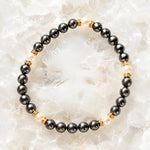 Jan Swarovski® Crystal Pearl Bracelet with gold crystal rondelles, black and cream Swarovski® Crystal Pearls, displayed on luminous white quartz crystals in a luxury flat lay jewelry photograph.
