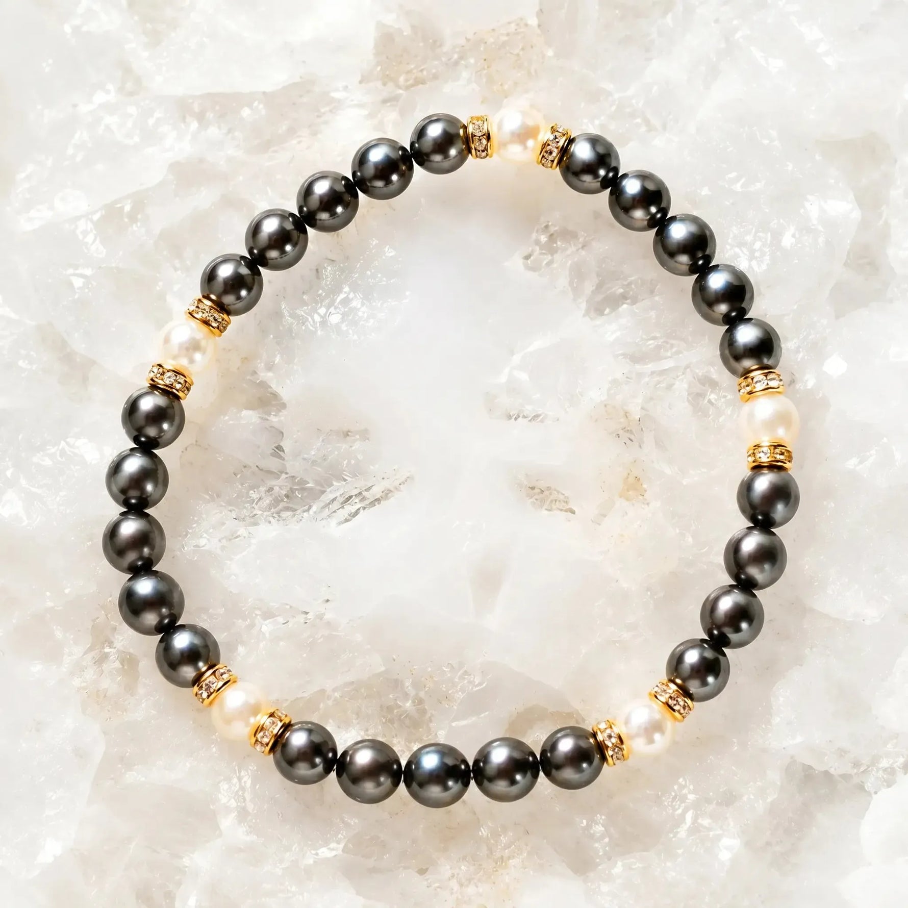 Jan Swarovski® Crystal Pearl Bracelet with gold crystal rondelles, black and cream Swarovski® Crystal Pearls, displayed on luminous white quartz crystals in a luxury flat lay jewelry photograph.