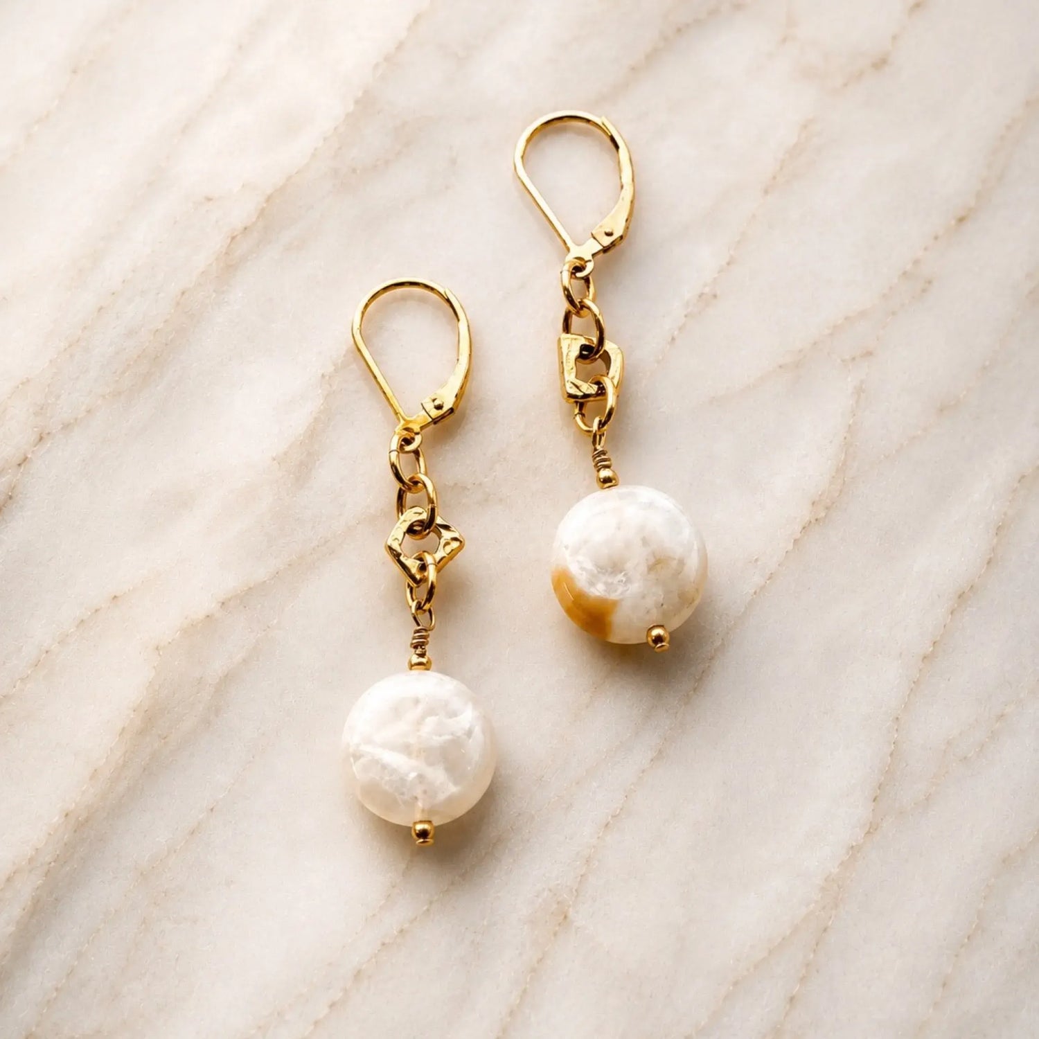 Jewel Cracked Agate Coin Earrings featuring genuine cracked agate gemstones and gold accents displayed on a soft ivory marble surface in a luxury product photograph.