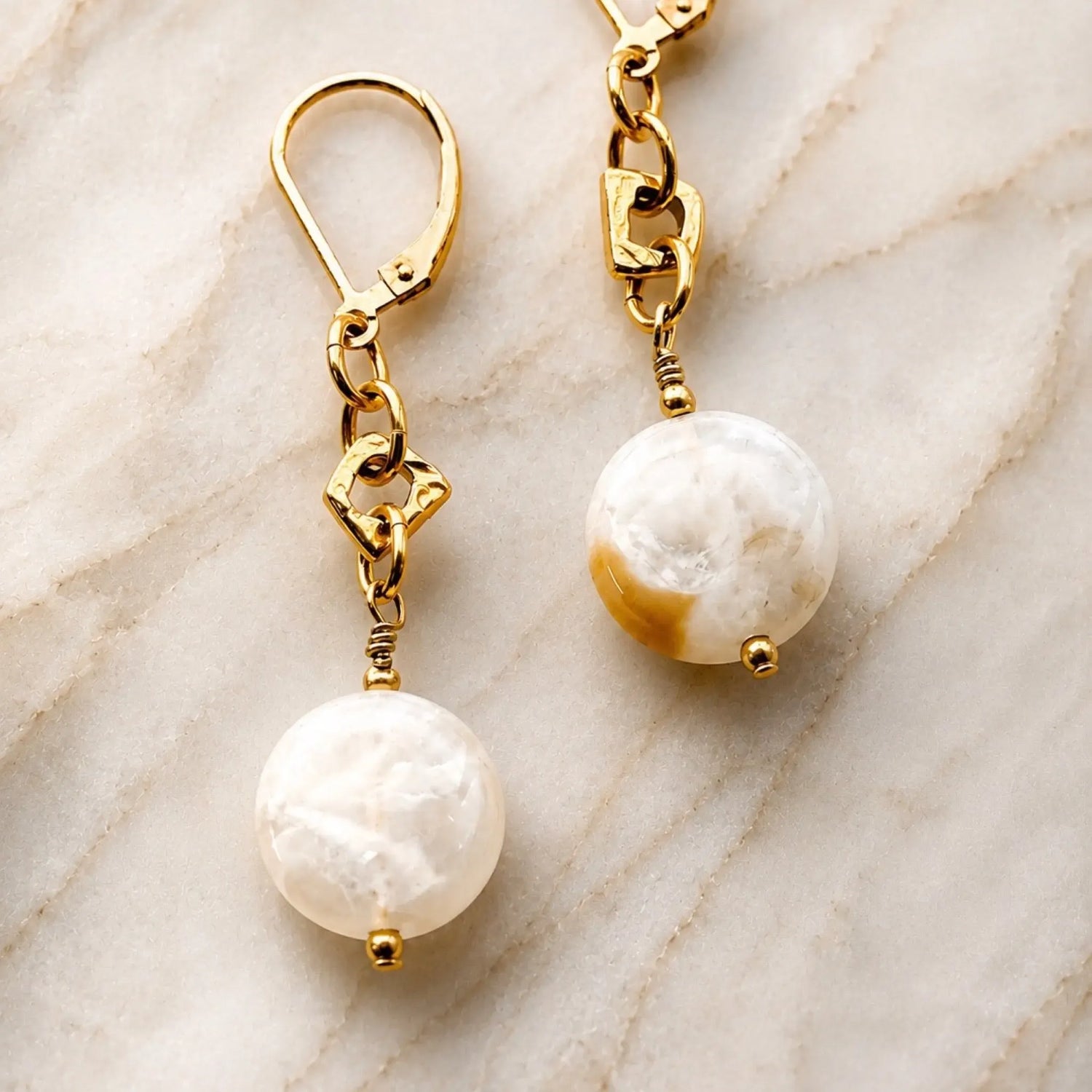 Luxury macro photograph of Jewel Cracked Agate Coin Earrings showcasing genuine cracked agate gemstones, gold-plated links, and 14k gold-filled lever back ear wires on a soft marble background.