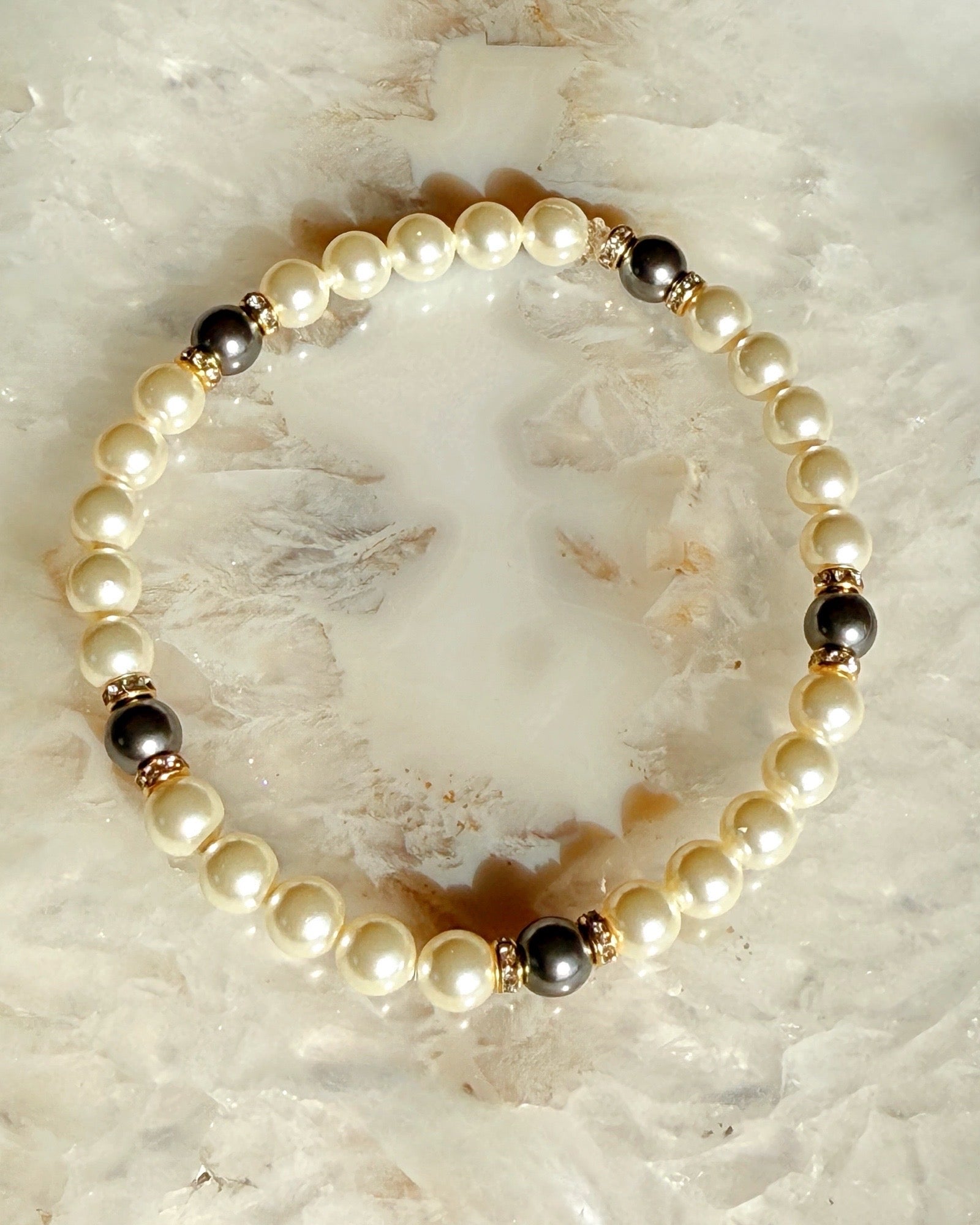 Juanita Pearl Stretch Bracelet featuring luminous cream pearl tones with deep charcoal accents and warm gold detailing, styled on natural stone for a timeless, refined look.
