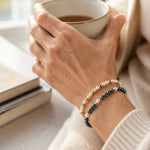 Kaia and Noelani Swarovski® Crystal Pearl Bracelets styled together on the wrist of an elegant woman in her 50s, featuring Tahitian, Moonlight, and cream Swarovski® Crystal Pearls with 14k gold-filled accents in a softly lit luxury setting.