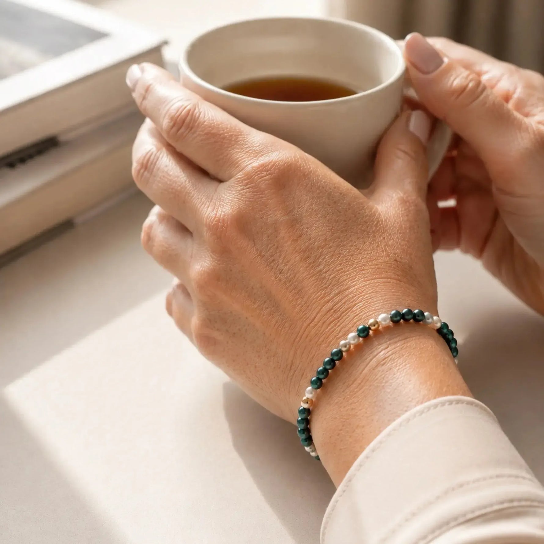 Kaia Swarovski® Crystal Pearl Bracelet worn during a relaxed coffee moment, featuring 4 mm Tahitian and Moonlight Swarovski® Crystal Pearls with 14k gold-filled accents in a softly lit luxury interior.