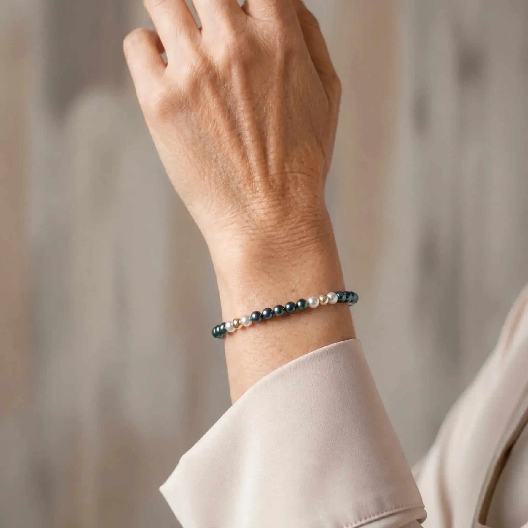 Kaia Swarovski® Crystal Pearl Bracelet worn by an elegant woman in her 50s, showcasing 4 mm Tahitian and Moonlight Swarovski® Crystal Pearls with 14k gold-filled accents in a refined editorial portrait.