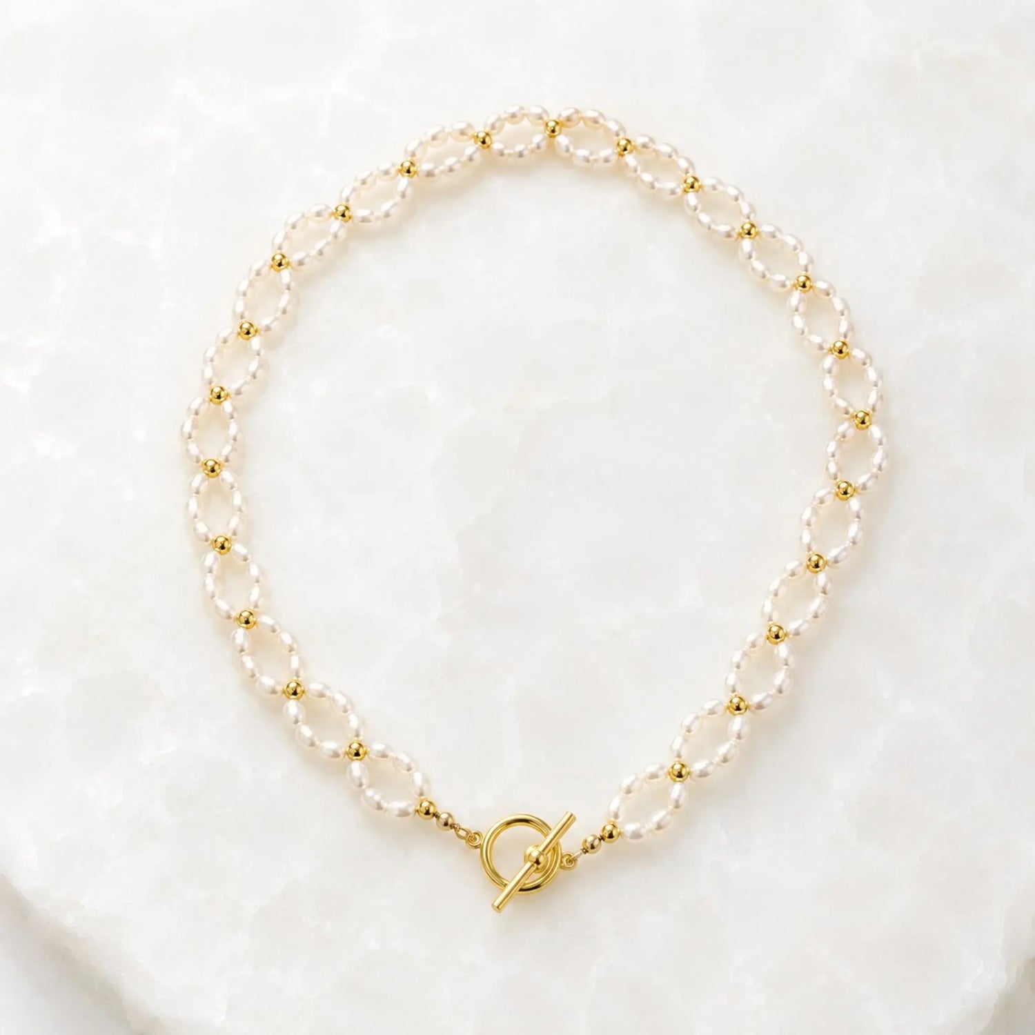 Kailani Freshwater Pearl Necklace handcrafted with freshwater rice pearls, champagne gold spacer beads, and a front toggle clasp displayed on the Carabella white quartz background.