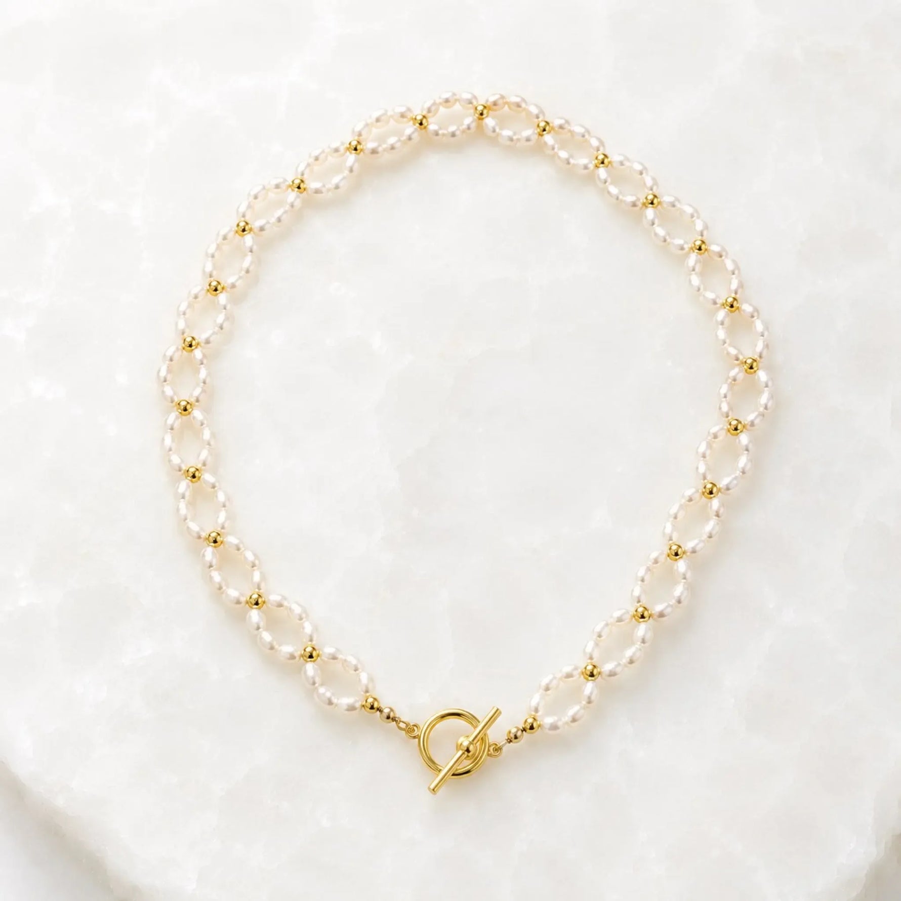 Kailani Freshwater Pearl Necklace handcrafted with freshwater rice pearls, champagne gold spacer beads, and a front toggle clasp displayed on the Carabella white quartz background.