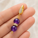 Kalei handcrafted amethyst gemstone earring resting across fingertips, showcasing its elegant scale, handcrafted construction, Austrian crystal rondelle, and 18k gold-plated CZ leverback.