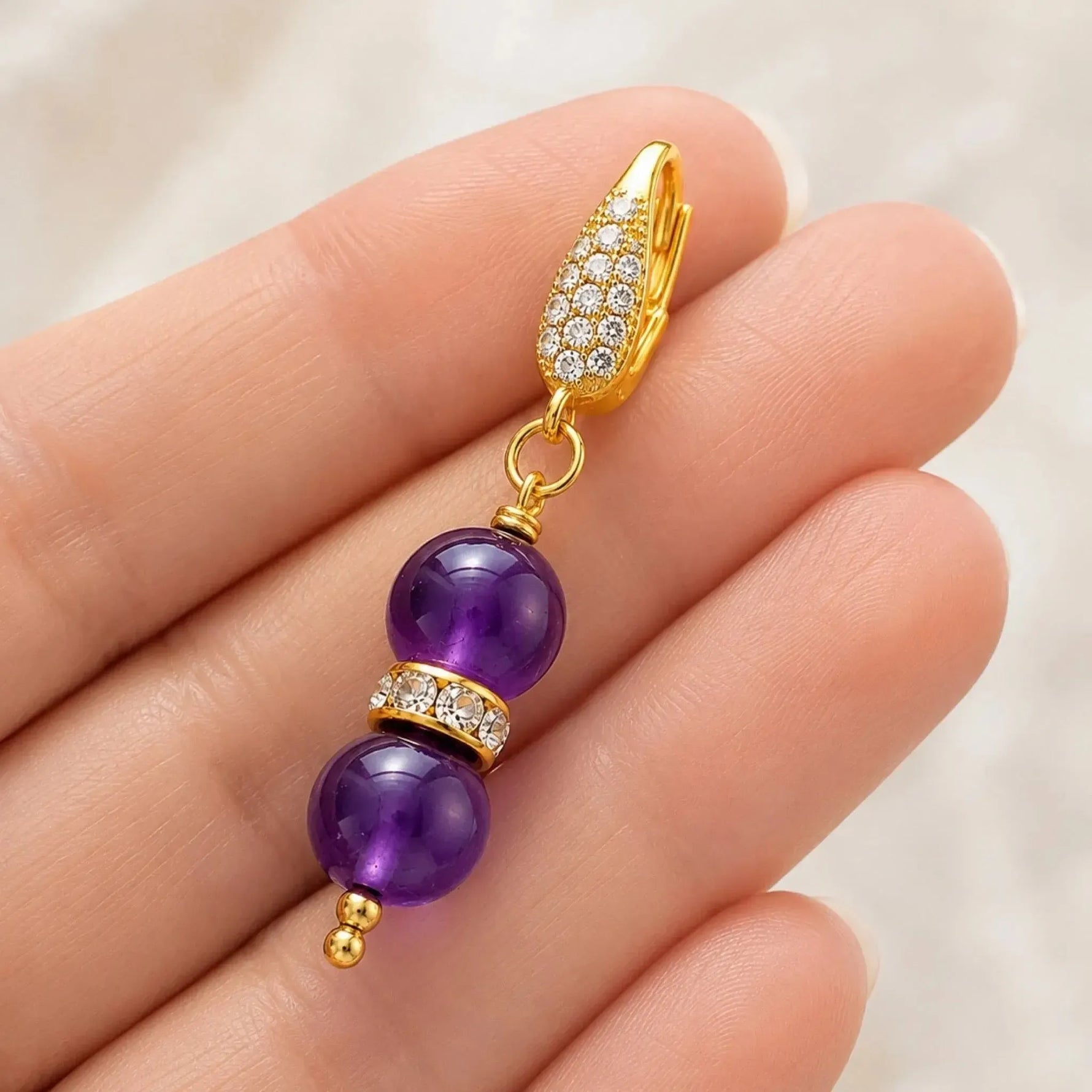 Kalei handcrafted amethyst gemstone earring resting across fingertips, showcasing its elegant scale, handcrafted construction, Austrian crystal rondelle, and 18k gold-plated CZ leverback.
