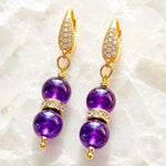 Kalei handcrafted amethyst gemstone earrings with Austrian crystal rondelles and 18k gold-plated CZ leverback earrings displayed on white crystal quartz.
