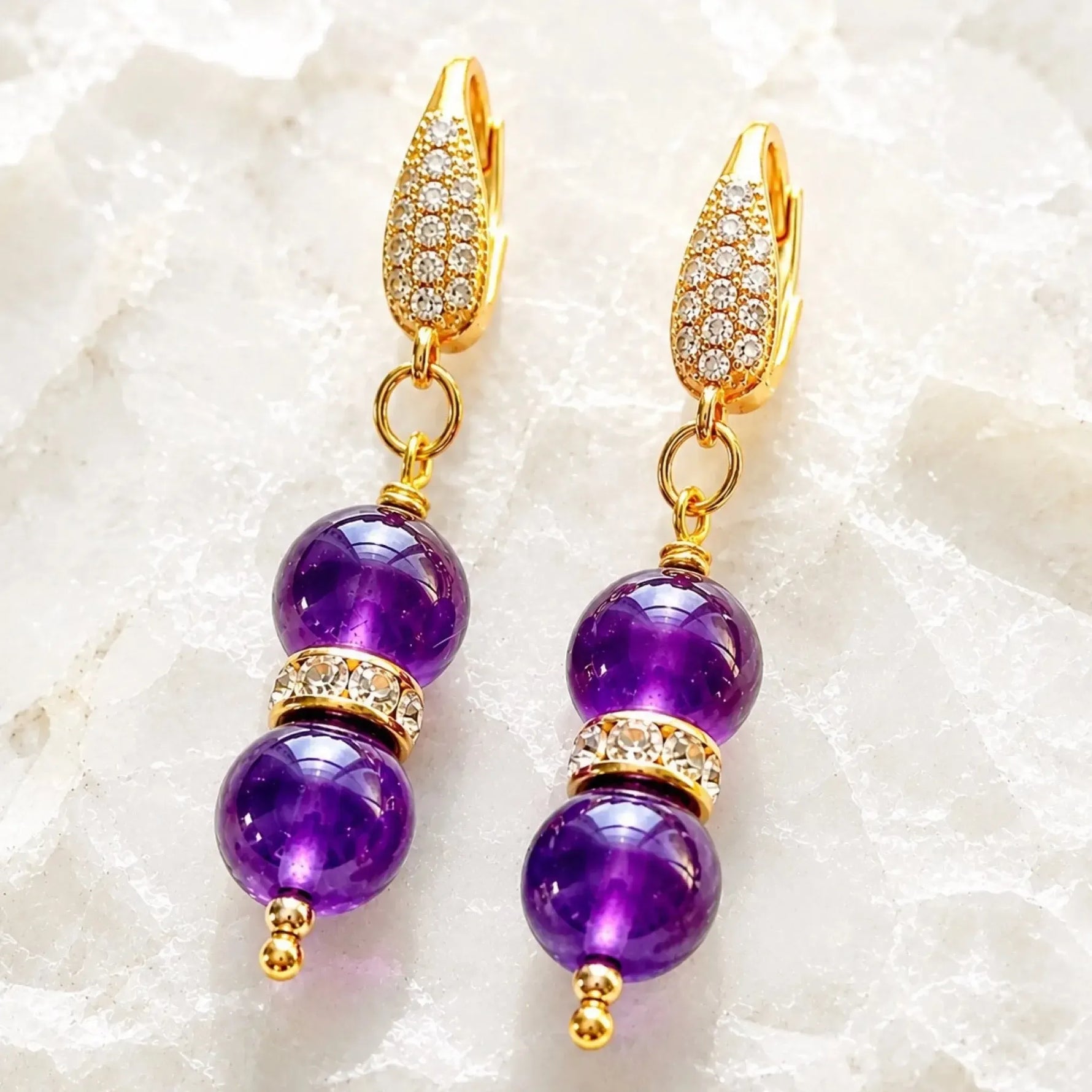 Kalei handcrafted amethyst gemstone earrings with Austrian crystal rondelles and 18k gold-plated CZ leverback earrings displayed on white crystal quartz.