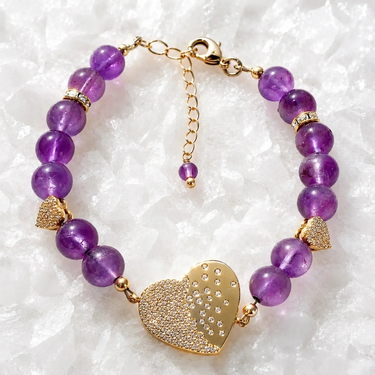 Kalei amethyst gemstone bracelet with pavé heart connector, Austrian crystal rondelles, gold heart charms, and polished gold clasp displayed on white quartz.