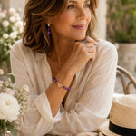Kalei amethyst bracelet and matching earrings worn by an elegant woman, featuring genuine amethyst gemstones, Austrian crystal rondelles, and gold accents in a refined outdoor editorial lifestyle portrait.