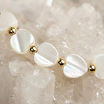 Macro detail of the Kalila Mother of Pearl Heart Bracelet featuring iridescent Mother of Pearl heart beads, polished 14k gold-filled beads, and sparkling quartz crystals.