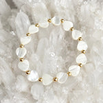 Kalila Mother of Pearl Heart Bracelet with polished 14k gold-filled accent beads displayed on a luminous white quartz crystal cluster in a luxury jewelry flat lay.