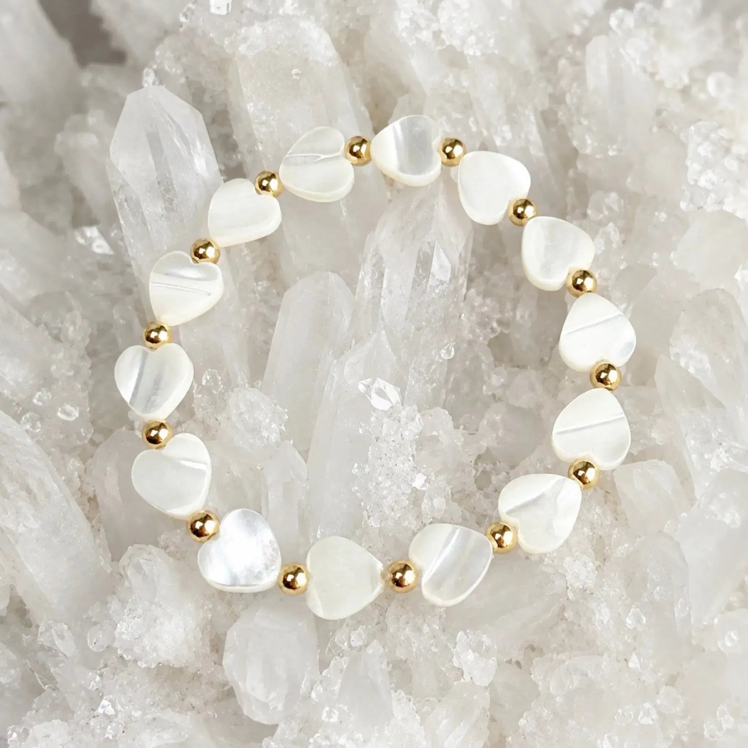 Kalila Mother of Pearl Heart Bracelet with polished 14k gold-filled accent beads displayed on a luminous white quartz crystal cluster in a luxury jewelry flat lay.