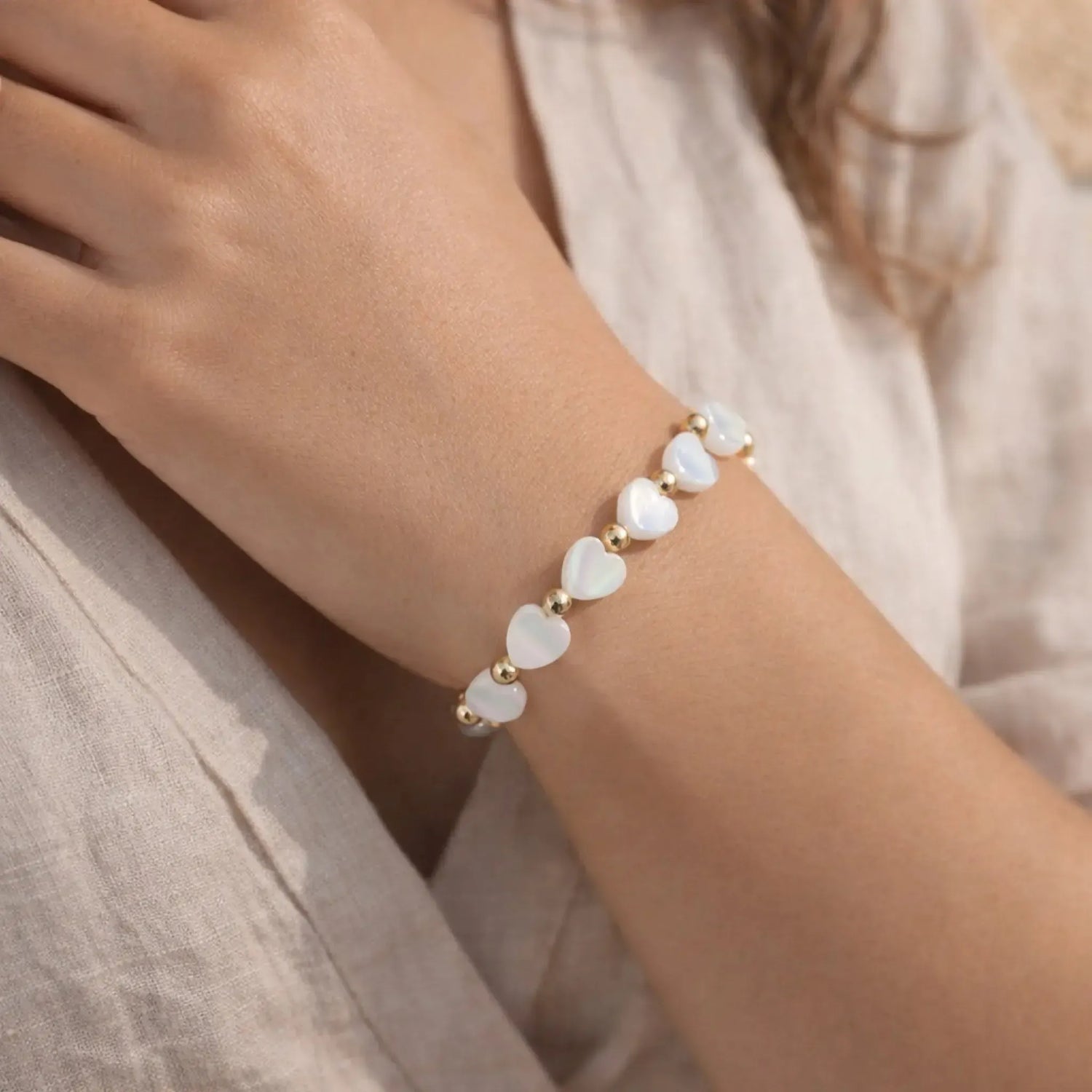 Close-up of the Kalila Mother of Pearl Heart Bracelet featuring luminous white Mother of Pearl heart beads and polished 14k gold-filled accent beads, worn on the wrist in a luxury beach setting with soft natural sunlight.