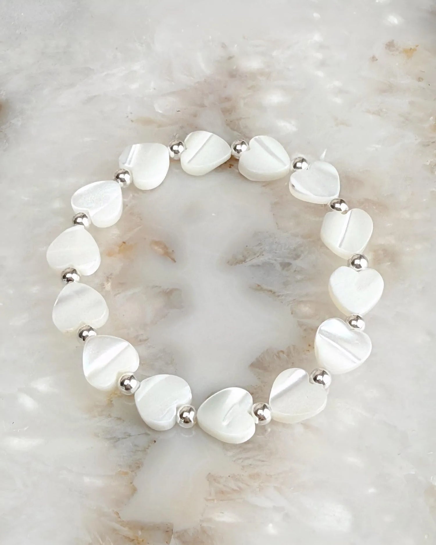 Kalila Mother of Pearl Heart Bracelet with delicate heart beads and silver accents on a natural stone background
