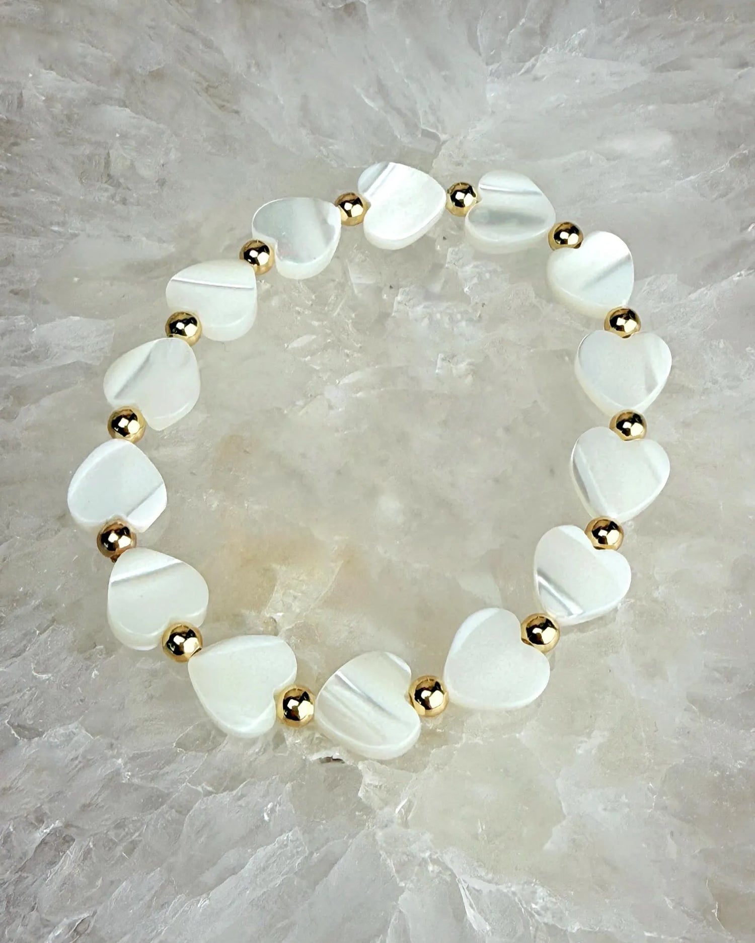 Kalila Mother of Pearl Heart Bracelet with delicate heart beads and gold accents on a natural stone background