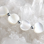Macro detail of the Kalila Mother of Pearl Heart Bracelet featuring luminous white Mother of Pearl hearts, polished sterling silver beads, and sparkling quartz crystal background.