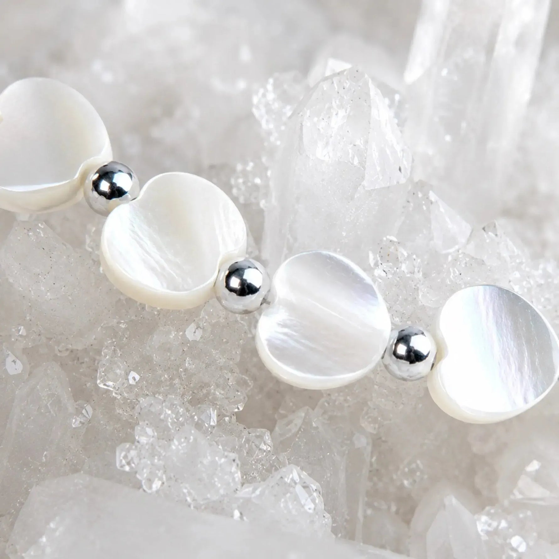 Macro detail of the Kalila Mother of Pearl Heart Bracelet featuring luminous white Mother of Pearl hearts, polished sterling silver beads, and sparkling quartz crystal background.