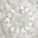 Kalila Mother of Pearl Heart Bracelet with sterling silver accent beads arranged on a luminous white quartz crystal cluster, luxury jewelry flat lay photograph.