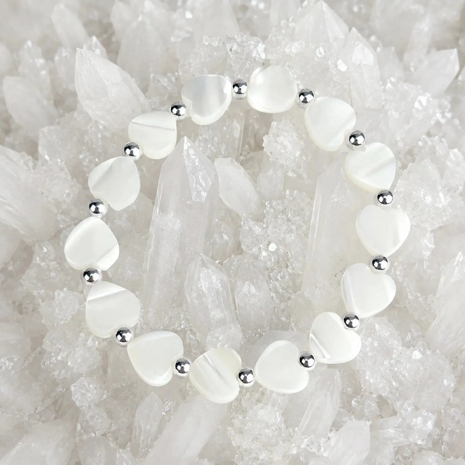 Kalila Mother of Pearl Heart Bracelet with sterling silver accent beads arranged on a luminous white quartz crystal cluster, luxury jewelry flat lay photograph.