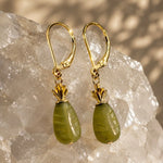 Layla carved jade drop earrings resting on raw crystal stone in warm natural light, featuring carved green jade and luminous gold accents.