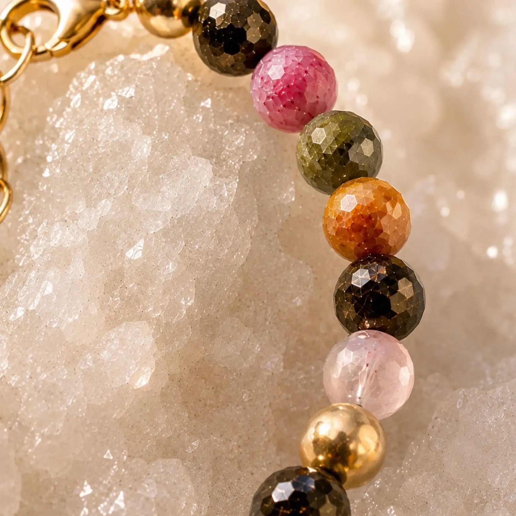 Macro detail of the Layla rainbow tourmaline bracelet highlighting faceted pink, olive green, amber, smoky brown, and blush tourmaline gemstones accented with polished gold beads on white quartz crystal.