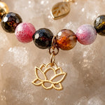 Macro close-up of the Layla rainbow tourmaline bracelet highlighting the gold lotus charm, faceted tourmaline gemstones, and warm gold accents resting on sparkling white quartz crystal.