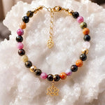 Layla rainbow tourmaline bracelet featuring multicolour faceted tourmaline gemstones, 14k gold accents, lotus charm, and leaf extender displayed on a white quartz crystal surface.