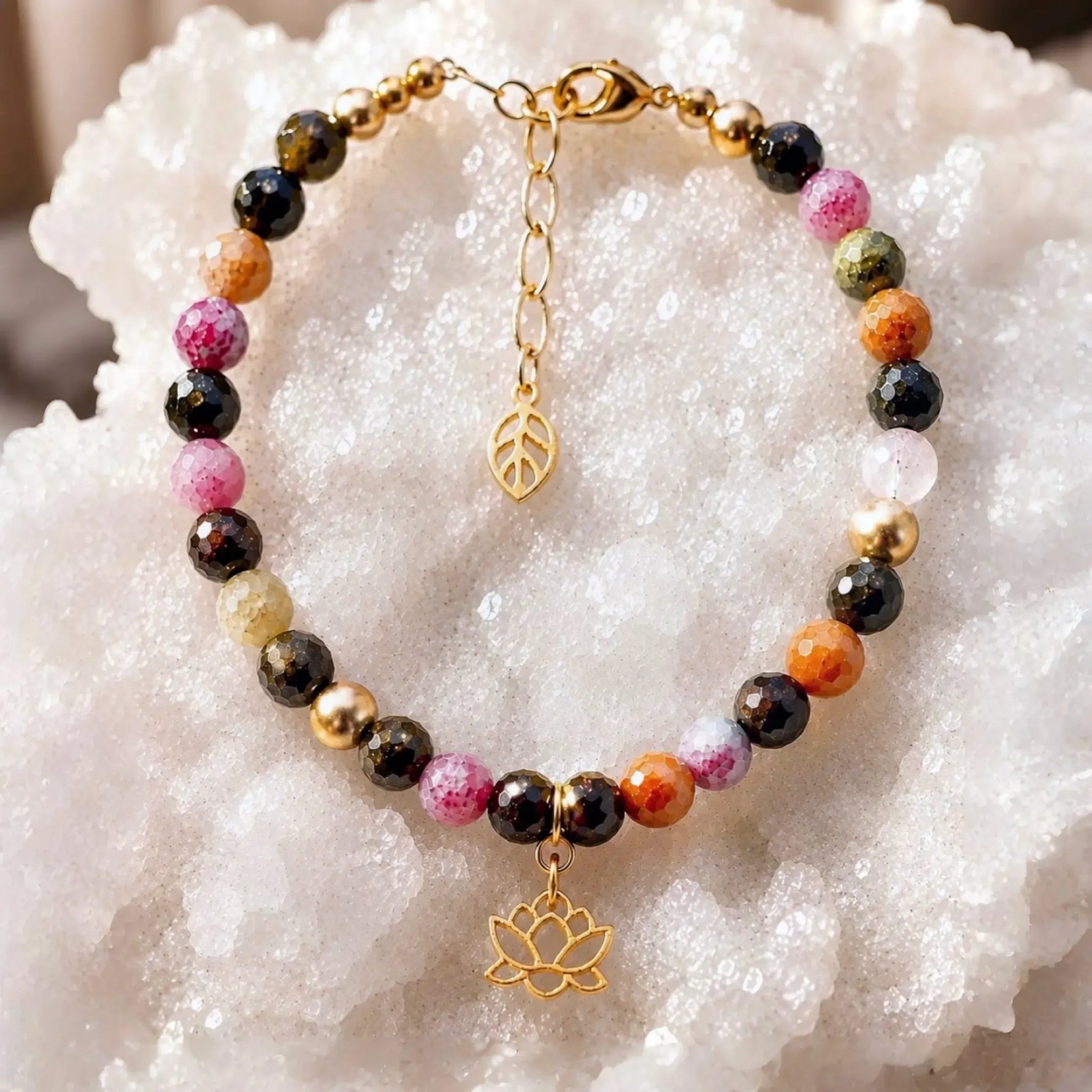 Layla rainbow tourmaline bracelet featuring multicolour faceted tourmaline gemstones, 14k gold accents, lotus charm, and leaf extender displayed on a white quartz crystal surface.