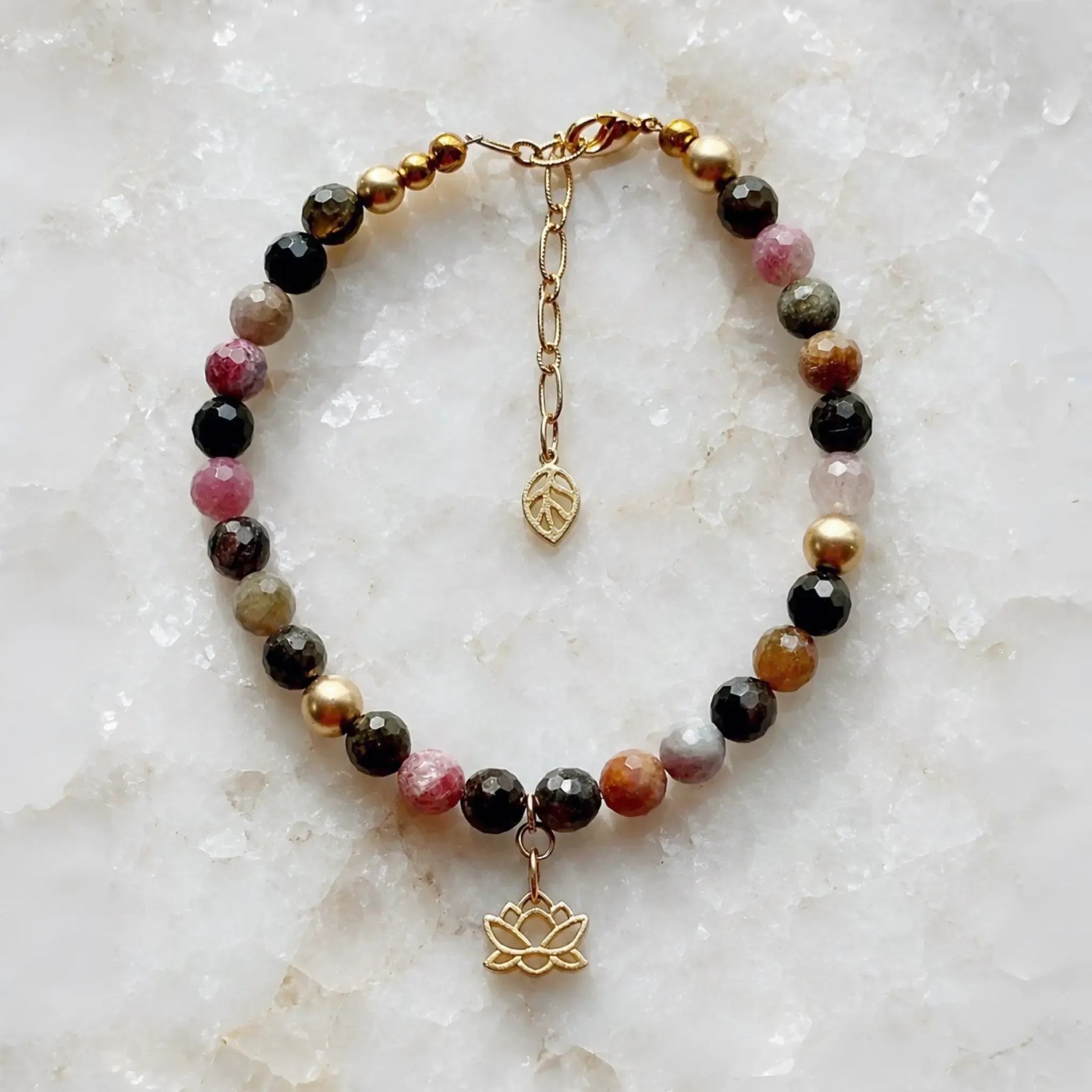 Layla Tourmaline Bracelet featuring faceted rainbow tourmaline gemstones, 14k gold accents, lotus charm, and adjustable extender chain displayed on a white quartz surface.
