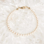 Leilani Swarovski® Crystal Pearl Bracelet resting on luminous white quartz crystal, featuring cream Swarovski® Crystal Pearls and a polished 14k gold clasp in a bright luxury flat lay.