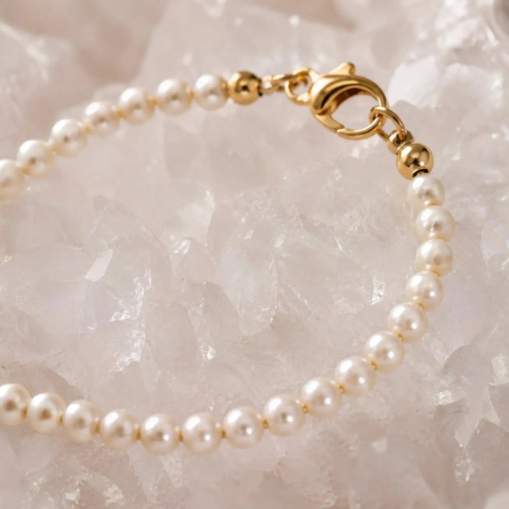 Macro detail of the Leilani Swarovski® Crystal Pearl Bracelet showcasing cream Swarovski® Crystal Pearls, polished gold clasp, and fine craftsmanship against luminous white quartz crystal.
