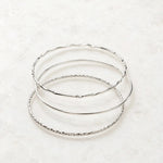 Lilith sterling silver bangles arranged on a white quartz background showcasing three handcrafted stackable bangles with polished, smooth, and hand-textured finishes.