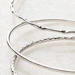 Macro detail of the Lilith handcrafted sterling silver bangles highlighting polished, organic, and hand-textured finishes on a white quartz background.