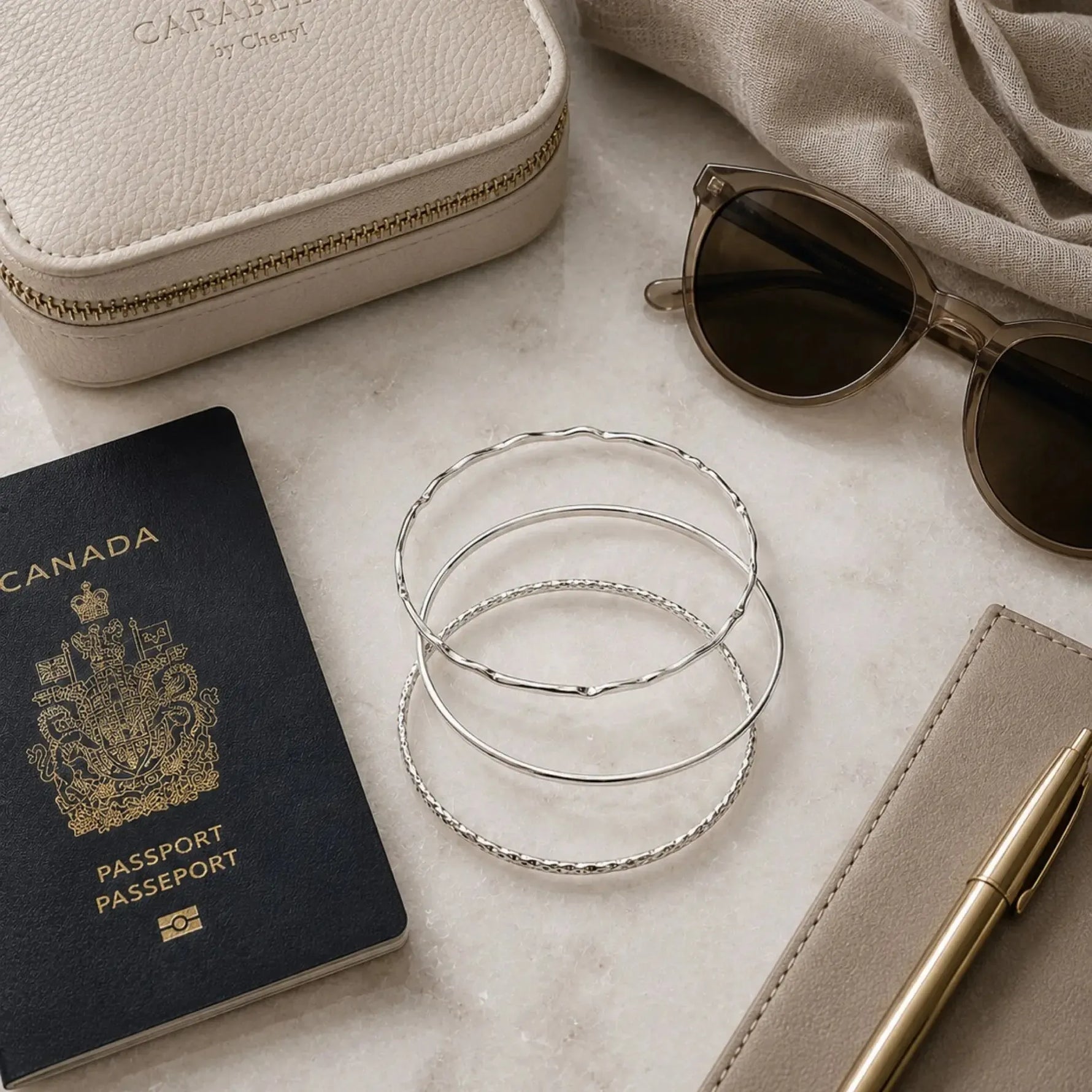 Lilith handcrafted sterling silver bangles styled with a passport, jewellery case, sunglasses, and travel accessories on a white quartz surface.